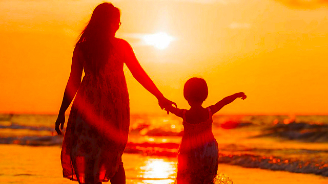 Mother and her little girl holding hands silhouette by a sunset on the beach
